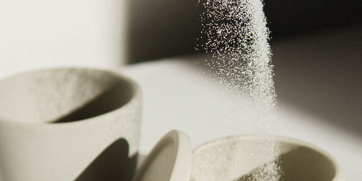 How Sugar Messes With Your Hormones After 40 from Wile. A spoon dusts white sugar into a light grey ceramic dish.