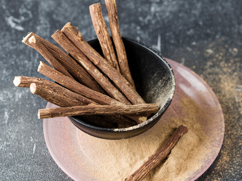 Licorice Root for PMS & Periods After 40 from Wile, a ceramic cup with licorice roots sits on a pink ceramic plate with ground and whole licorice root. 