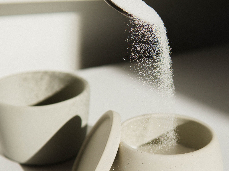 How Sugar Messes With Your Hormones After 40 from Wile. A spoon dusts white sugar into a light grey ceramic dish.