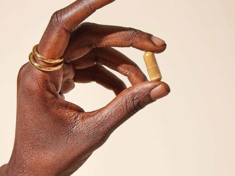 hand of a black woman holding a Wile Supplement capsule 