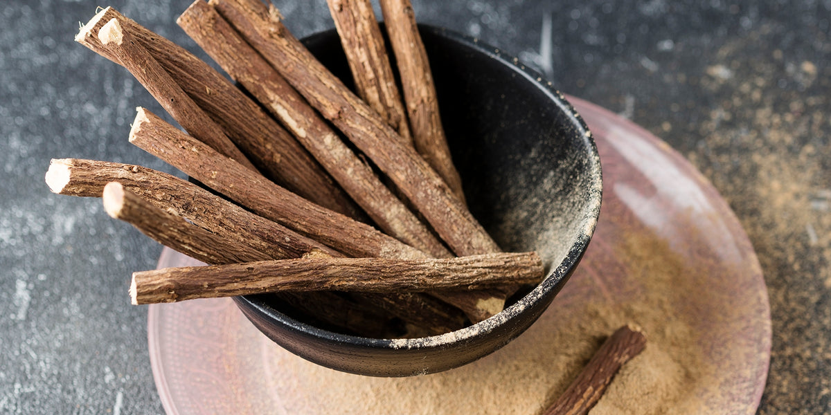 Licorice Root for PMS & Periods After 40 from Wile, a ceramic cup with licorice roots sits on a pink ceramic plate with ground and whole licorice root. 