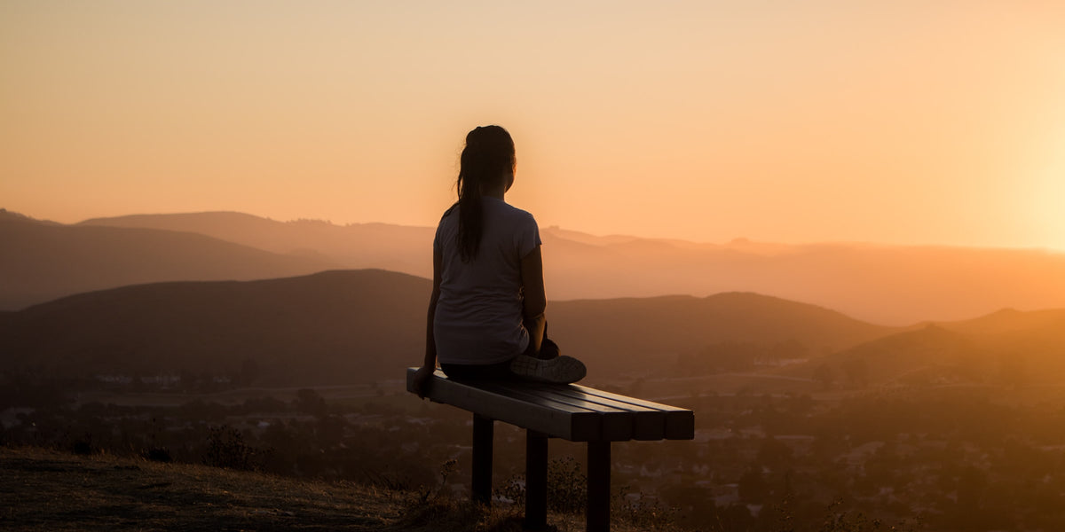 What is the Best Natural Remedy for Stress and Anxiety from Wile, a woman sits on a bench and watches the sunset